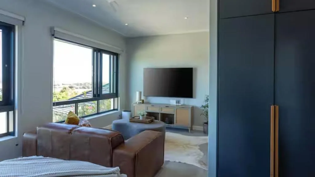 Modern lounge with brown sofa, wall-mounted TV, and expansive windows overlooking landscape