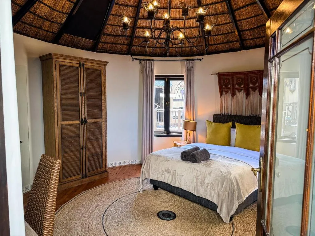 Circular bedroom with thatched roof, queen bed, yellow pillows, wooden wardrobe