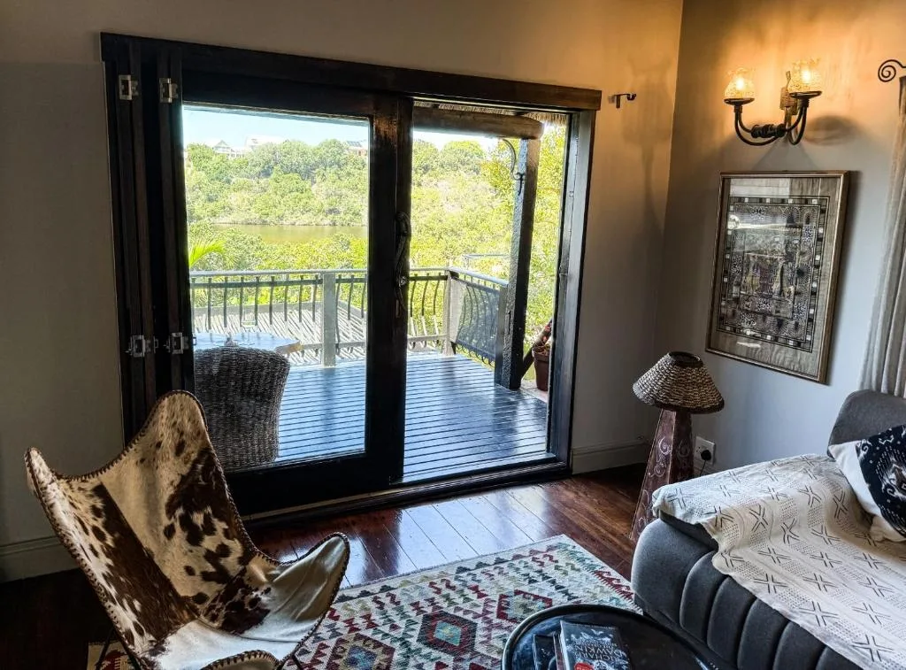 Bedroom with bed, cowhide chair, and lagoon views through glass doors