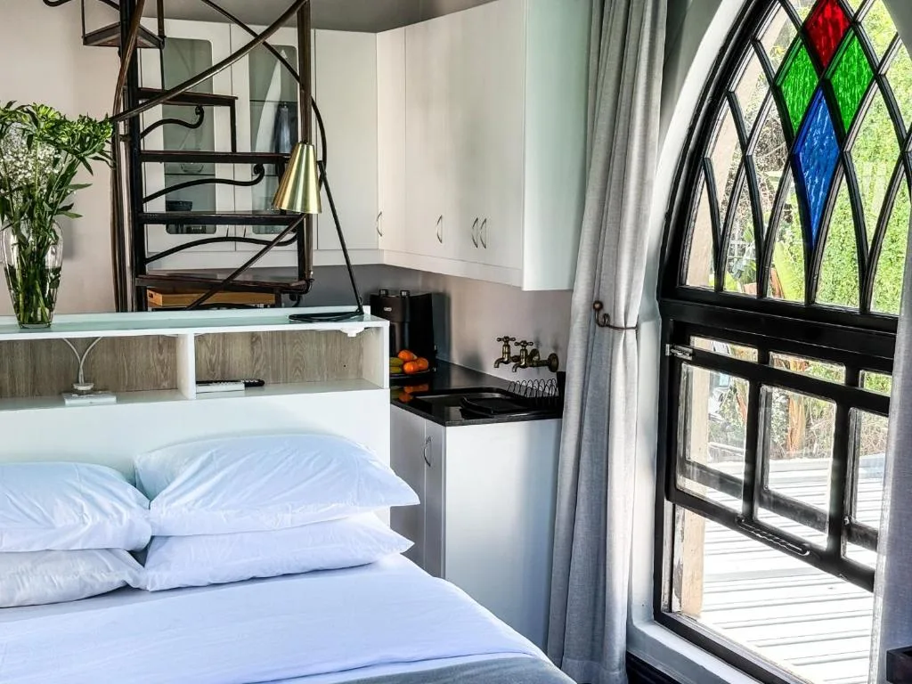 Bedroom with white pillows, built-in desk, and colorful stained glass door