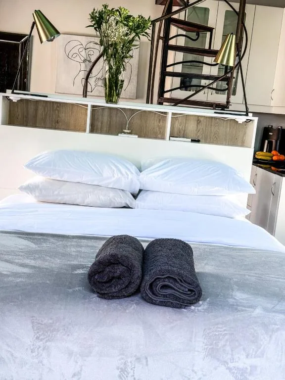 Freshly made bed with white pillows and rolled dark towels displayed