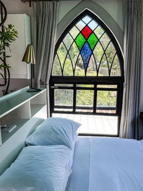 Bedroom with bed facing decorative stained glass window overlooking garden