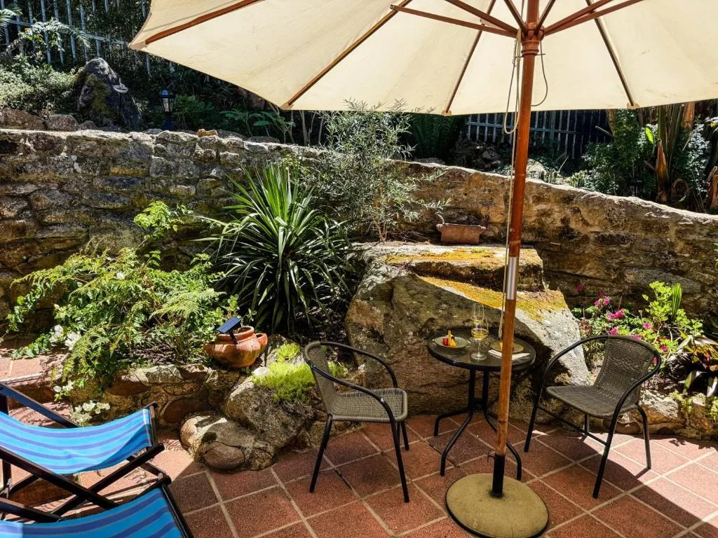 Shaded outdoor patio with chairs, umbrella, and lush garden surroundings