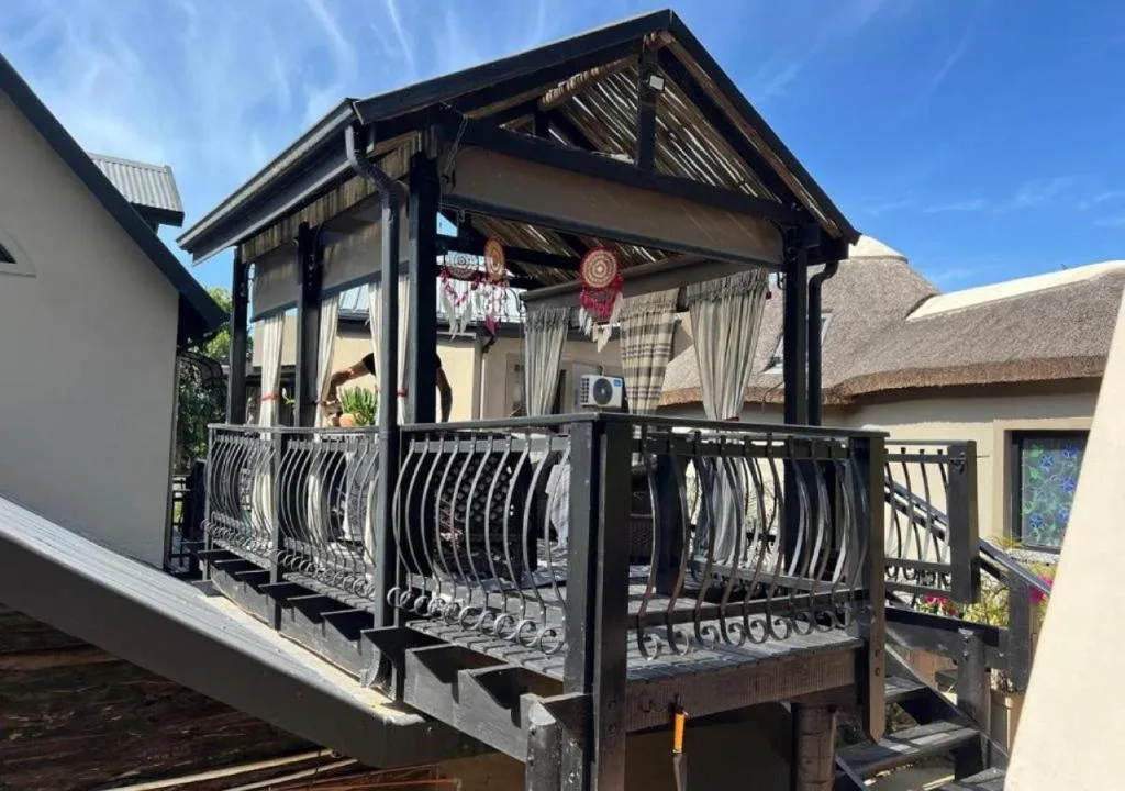 Covered wooden deck with black railings and cream curtains overlooking gardens