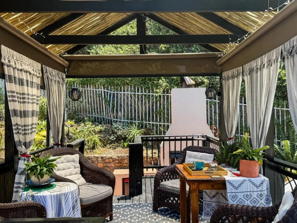 Covered outdoor deck with comfortable seating, potted plants, and garden views