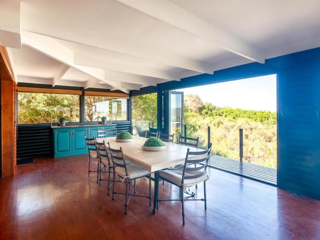 Modern dining area with white table, blue kitchen, and garden views