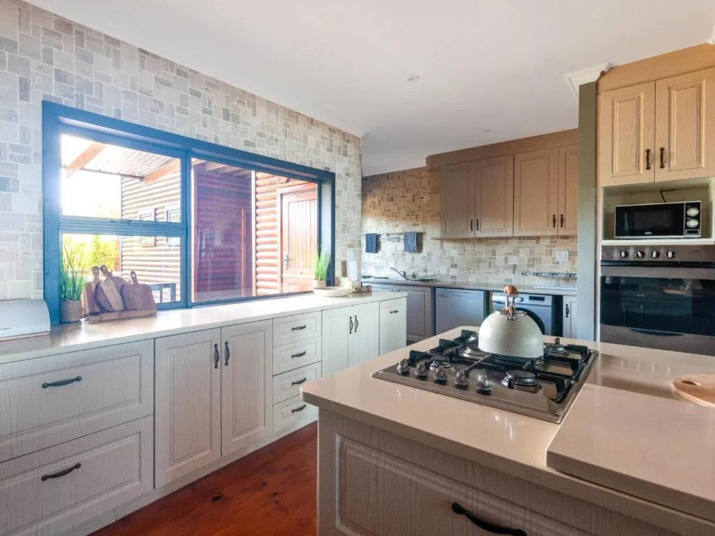 Modern kitchen with cream cabinetry, gas cooktop, and garden window view