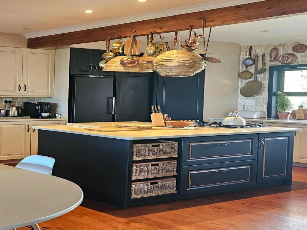 Modern kitchen with black island, wooden countertop, hanging copper cookware and beamed ceiling