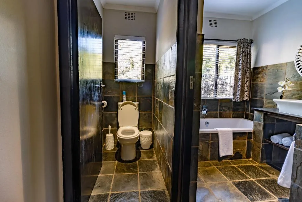 Modern bathroom with dark slate tiles, toilet, vanity sink, and bathtub