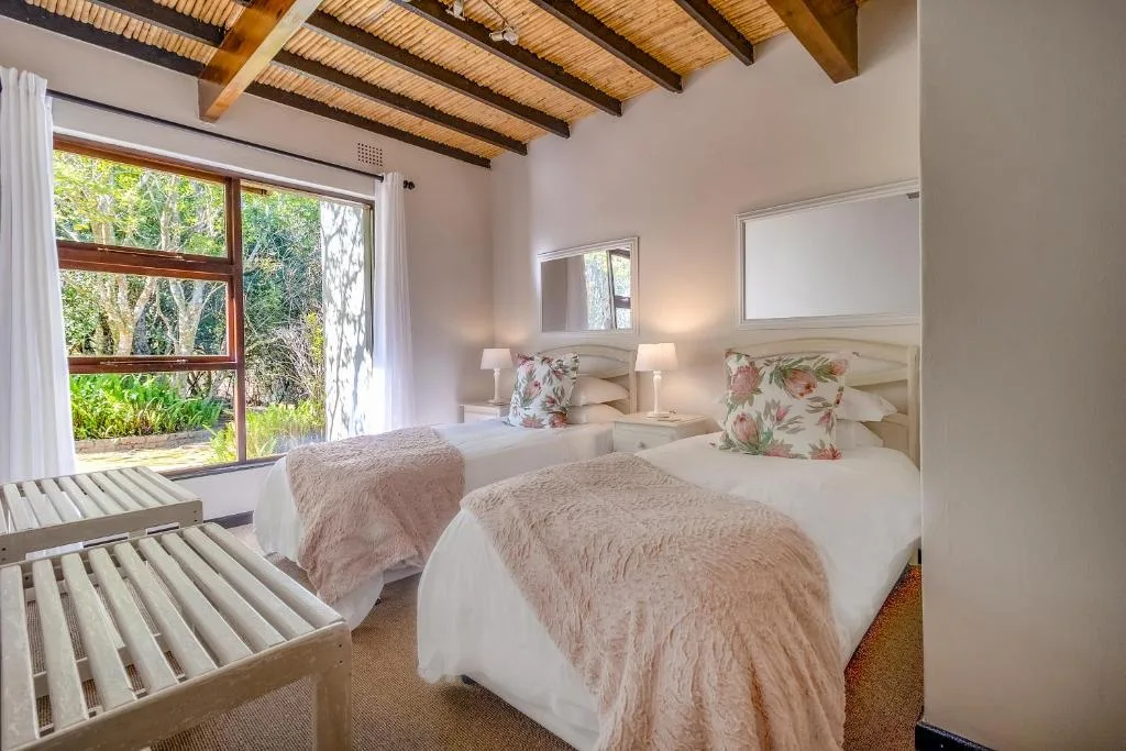Bright bedroom with twin beds, exposed wooden beams, garden views through large windows
