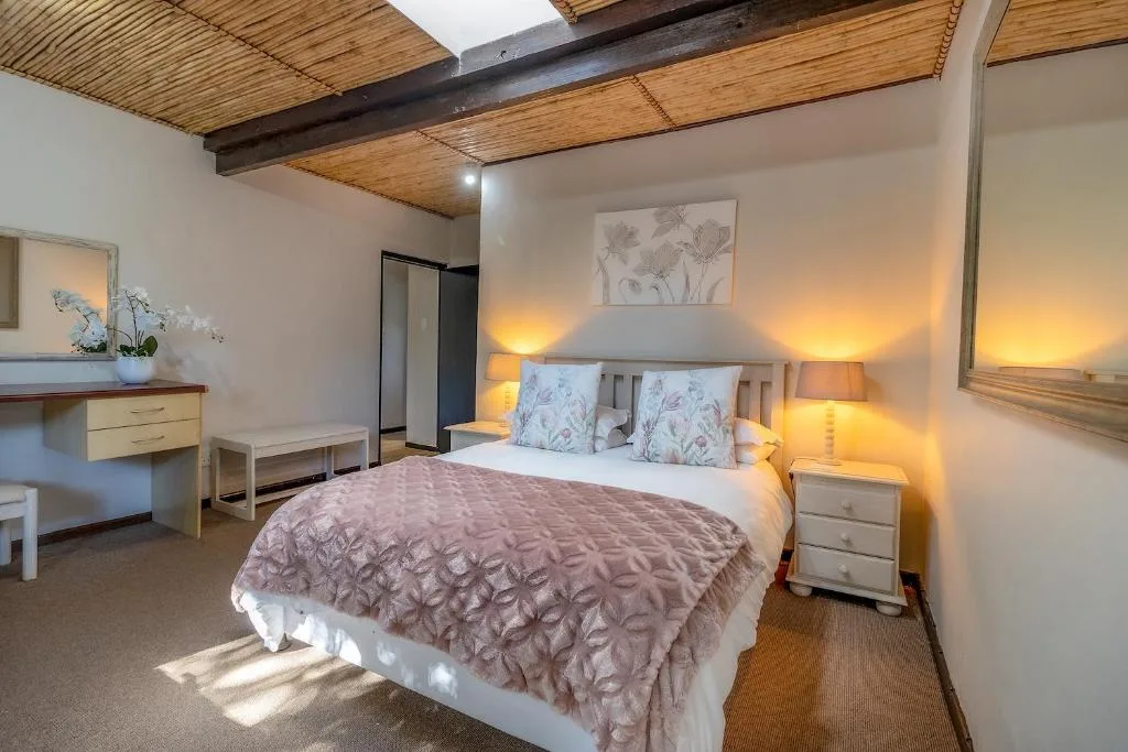 Spacious bedroom with queen bed, wooden beams, warm lighting, and garden view