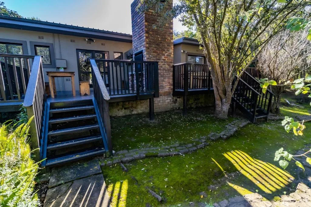 Modern chalet with blue deck stairs and black railings surrounded by lush green gardens