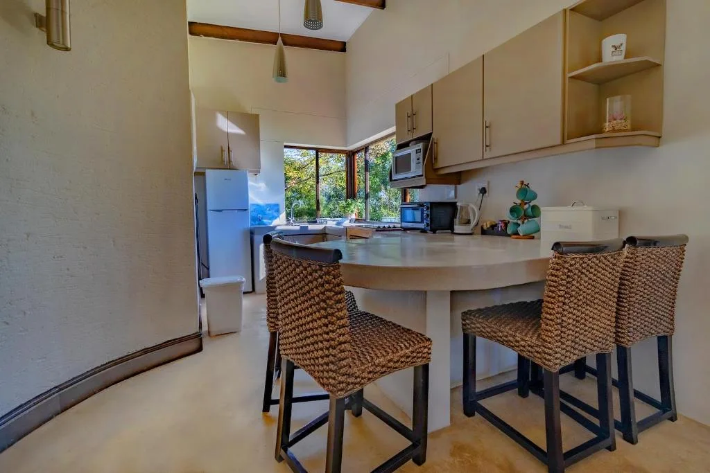 Modern kitchen with curved counter, woven chairs, and garden views through windows