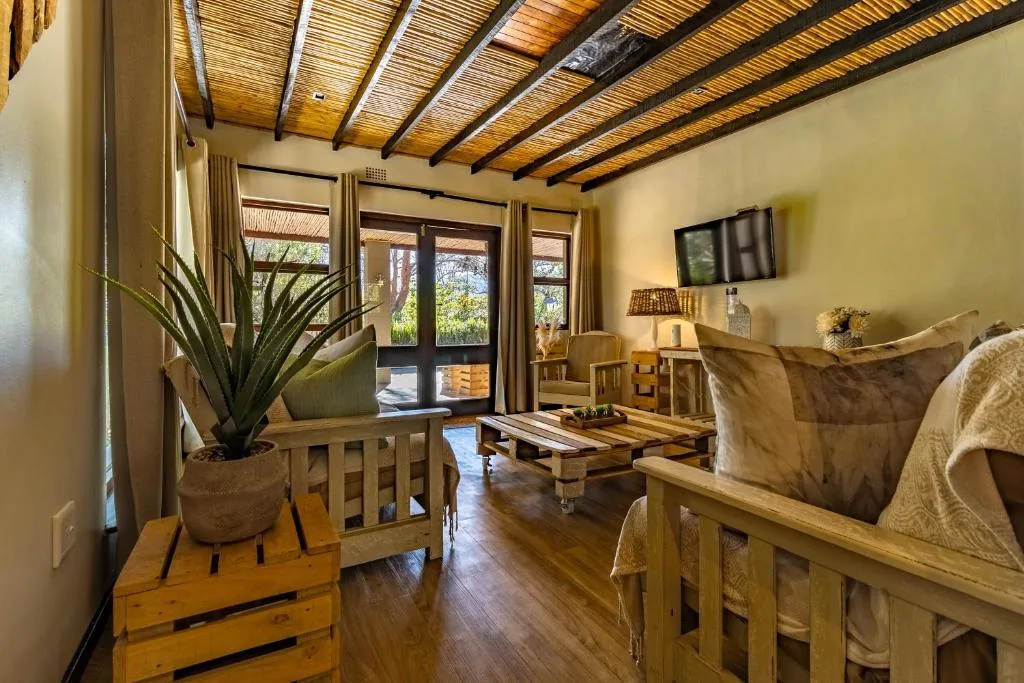Bright lounge with wooden beams, sofa, TV, and garden views through doors
