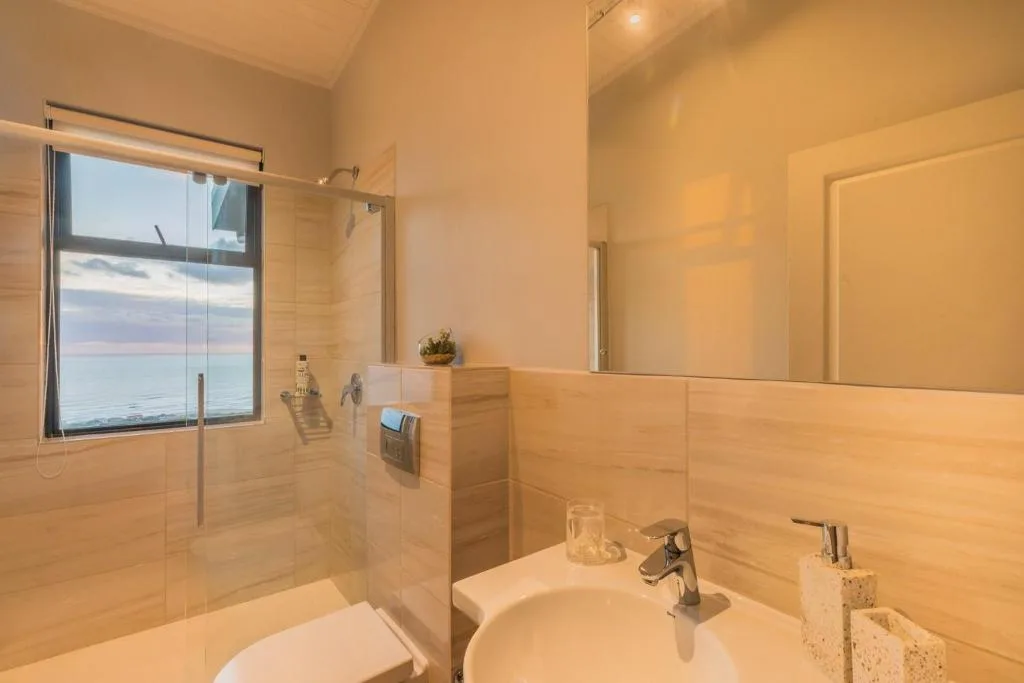 Modern bathroom with ocean view window, walk-in shower, and vanity sink