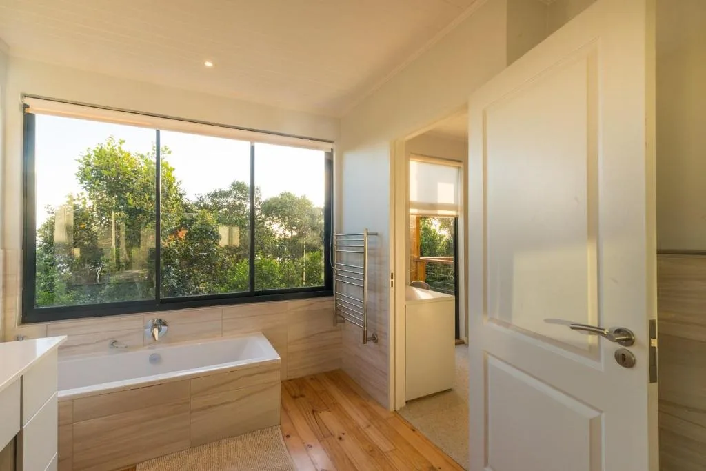 Modern bathroom with bathtub, large windows overlooking garden trees