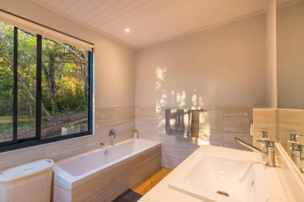 Modern bathroom with soaking tub, dual vanity, and forest views through window