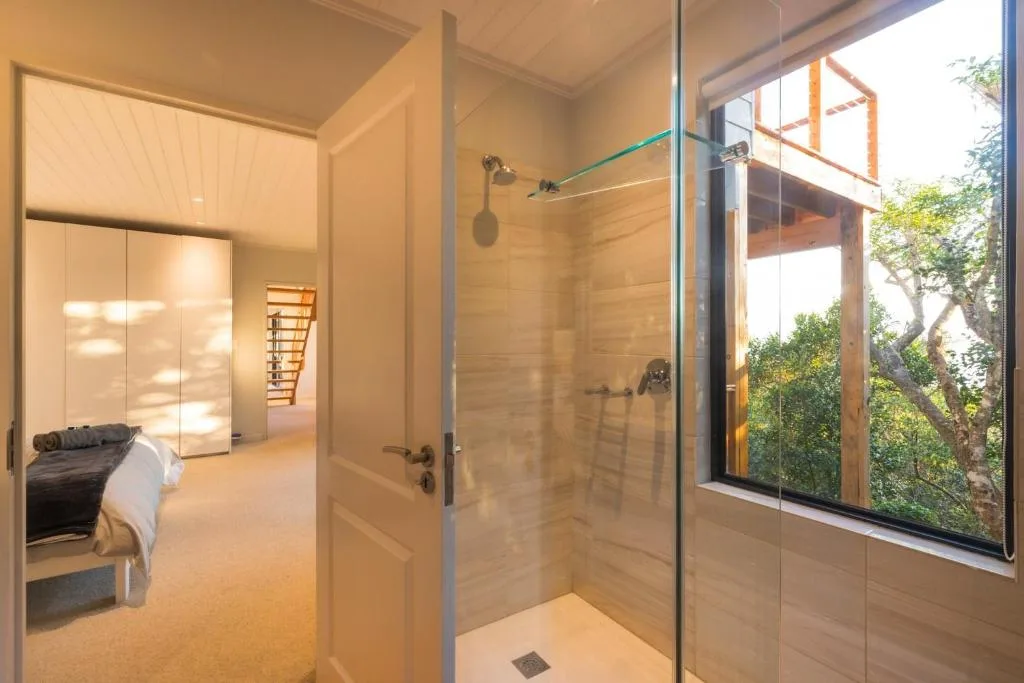Modern bathroom with walk-in shower, glass enclosure, and garden views through window