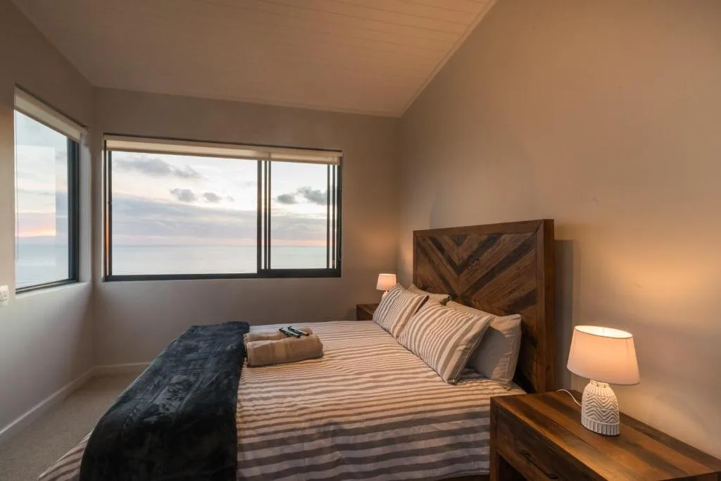 Bedroom with wooden headboard, striped bedding, ocean view through windows