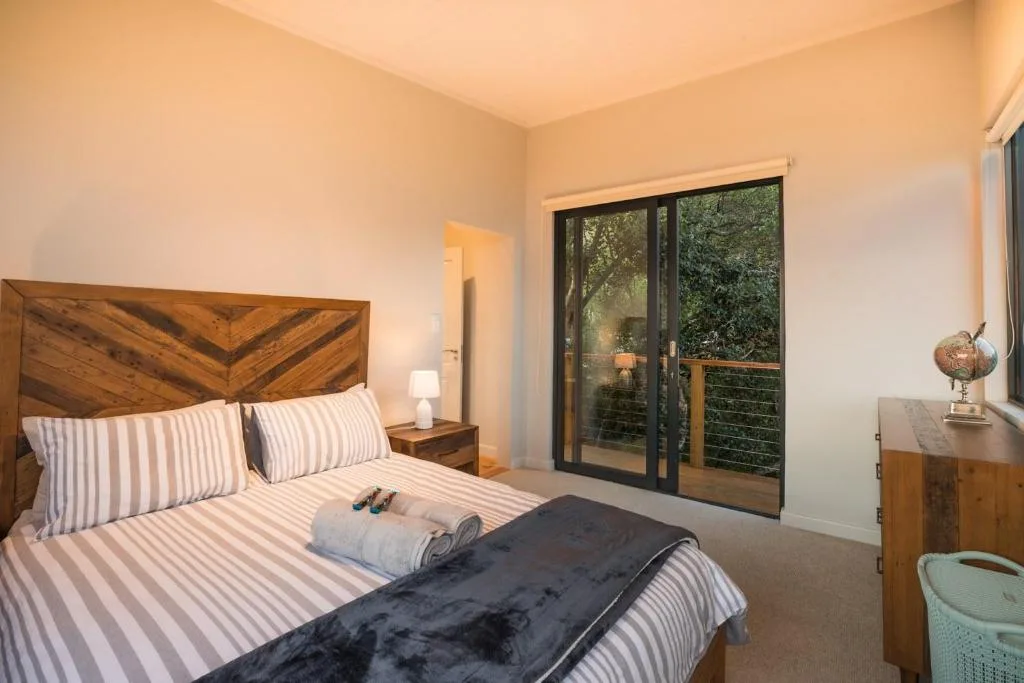 Spacious bedroom with wooden headboard, striped bedding, and garden views through glass doors