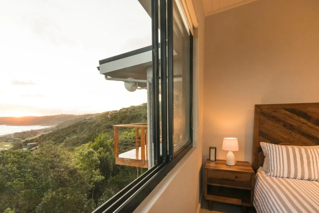 Bedroom with wooden bed, nightstand lamp, and panoramic water view through large windows