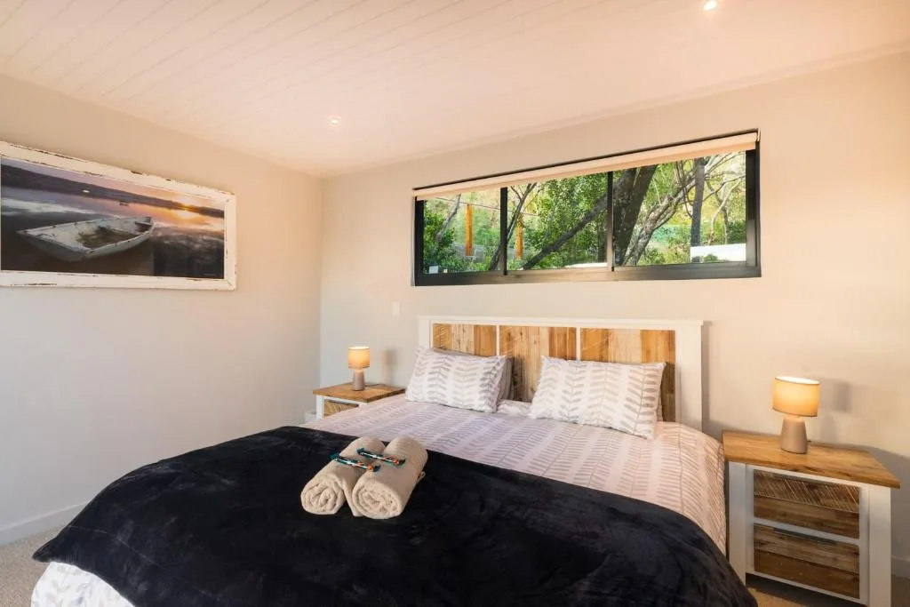 Bright bedroom with queen bed, wooden headboard, and garden views through windows