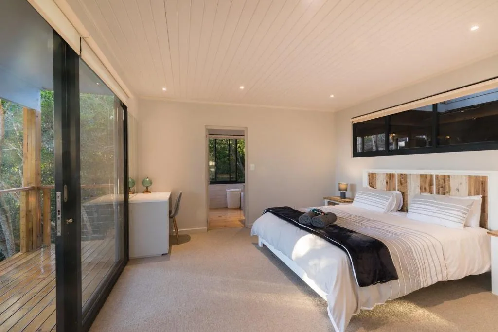 Spacious modern bedroom with king bed, large windows overlooking garden views