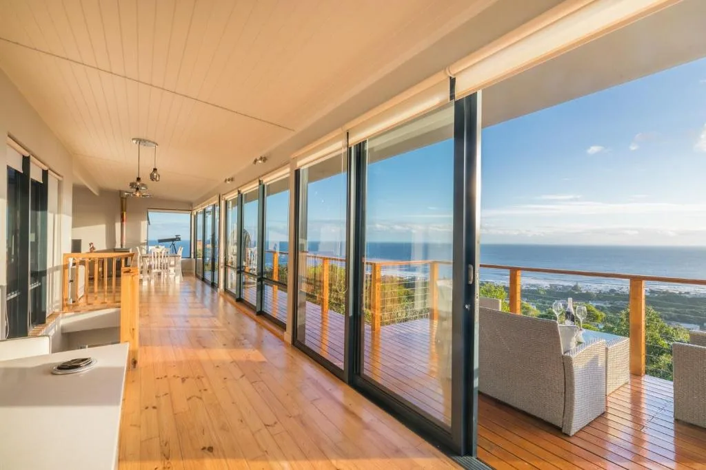 Spacious covered deck with ocean views, wooden flooring, and glass railings