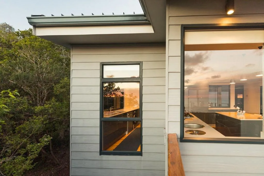 Modern villa exterior with large windows overlooking garden at sunset