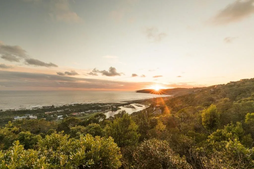 Sunset over coastal lagoon with forested hillside and ocean horizon