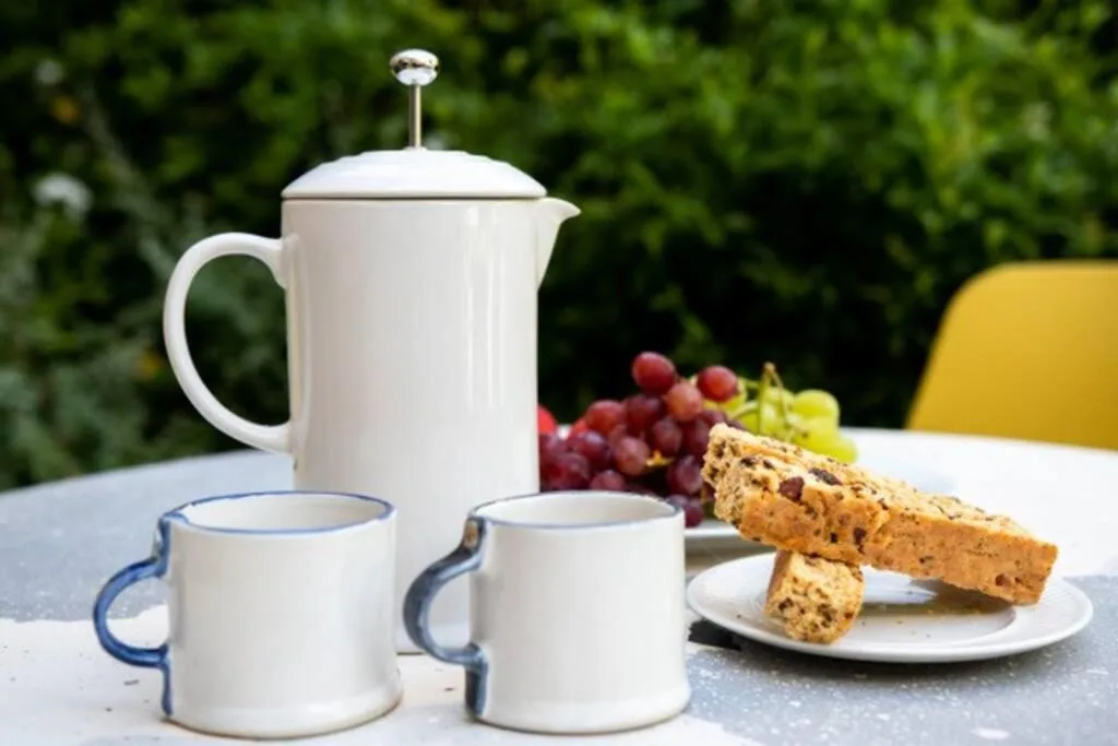 Outdoor breakfast setup with teapot, cups, fresh grapes, and biscotti on table