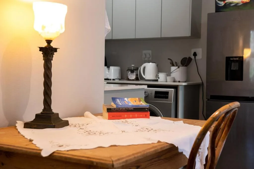 Open-plan dining area with table, lamp, books, and kitchen visible behind