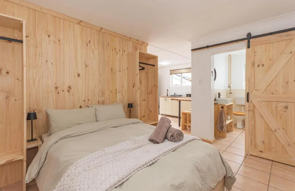 Bright bedroom with queen bed, wooden walls, and ensuite bathroom visible
