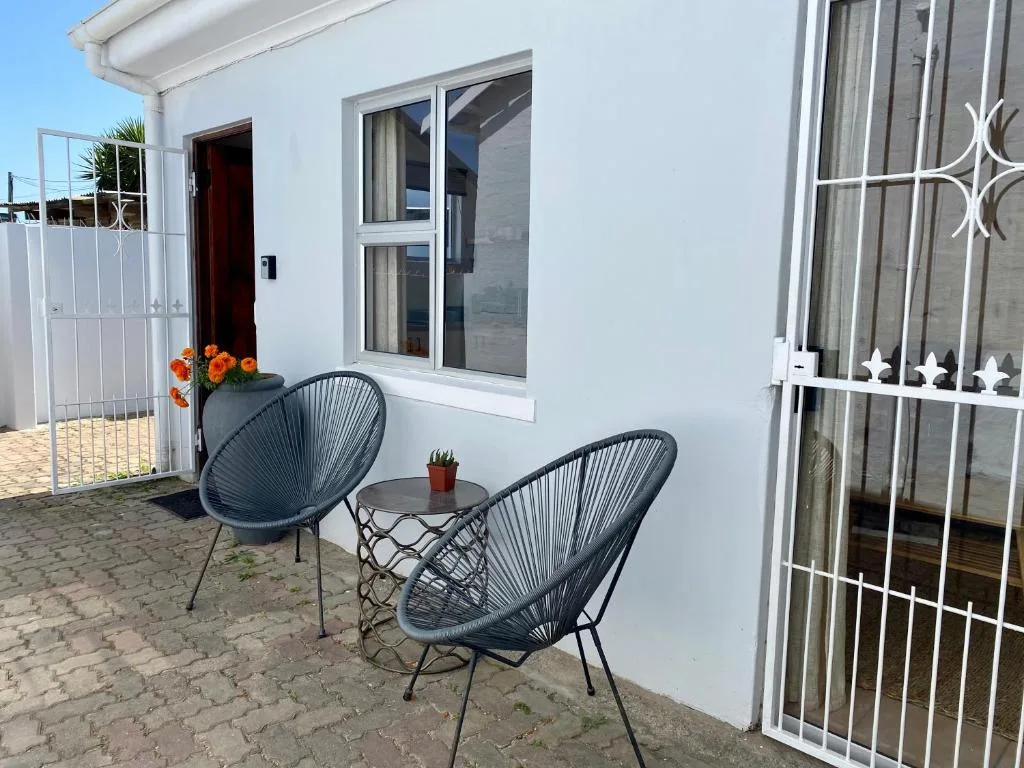 Outdoor patio with two dark woven chairs and small table, white cottage exterior