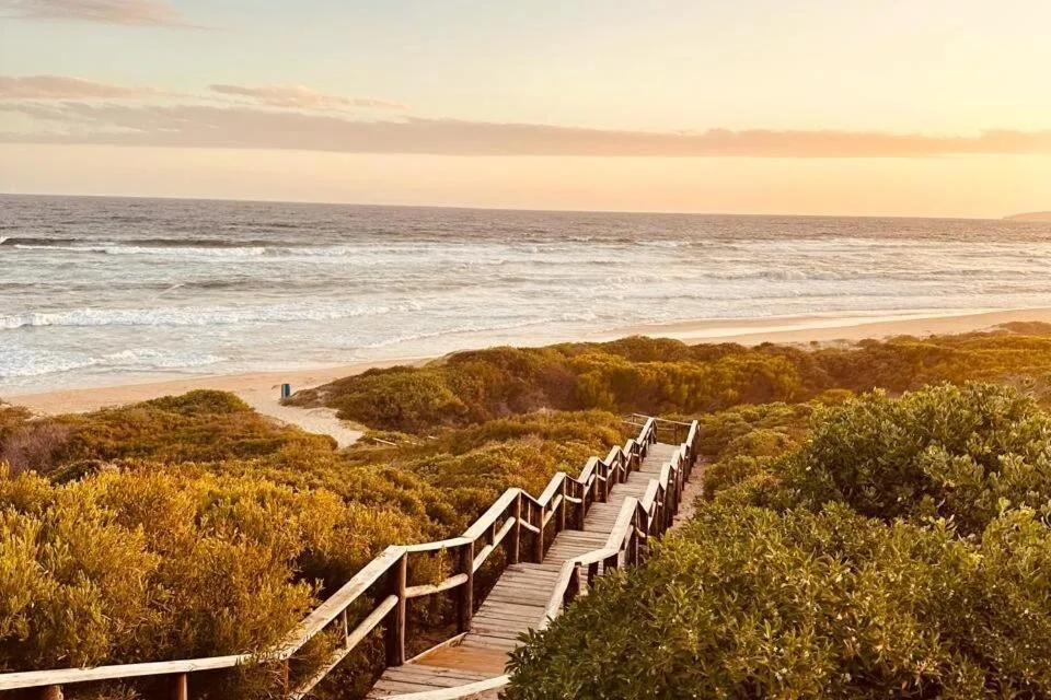 Wooden boardwalk descends toward golden beach and ocean at sunset