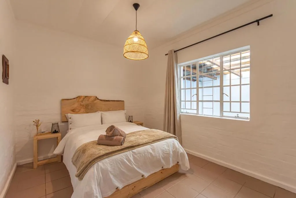 Bright bedroom with wooden bed, white linens, woven pendant light, and sea views