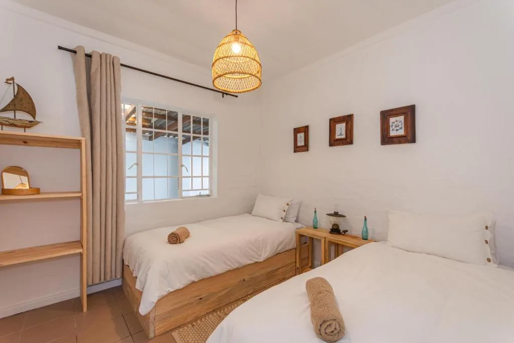 Bright bedroom with two single wooden beds, woven pendant light, coastal décor