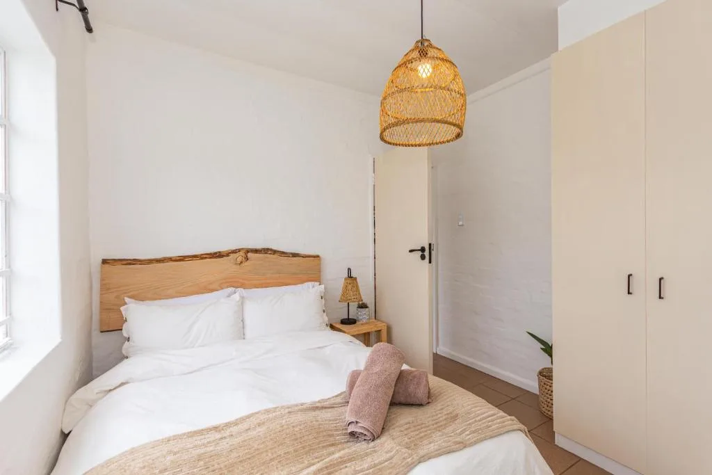 Modern bedroom with white bedding, wooden headboard, woven pendant light