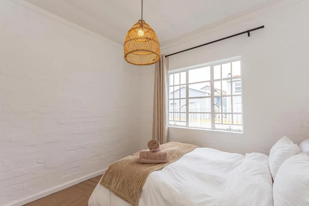 Bright bedroom with white linens, woven pendant light, and large window