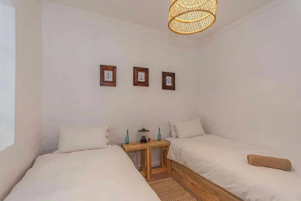 Twin bedroom with white linens, wooden nightstand, framed nautical art