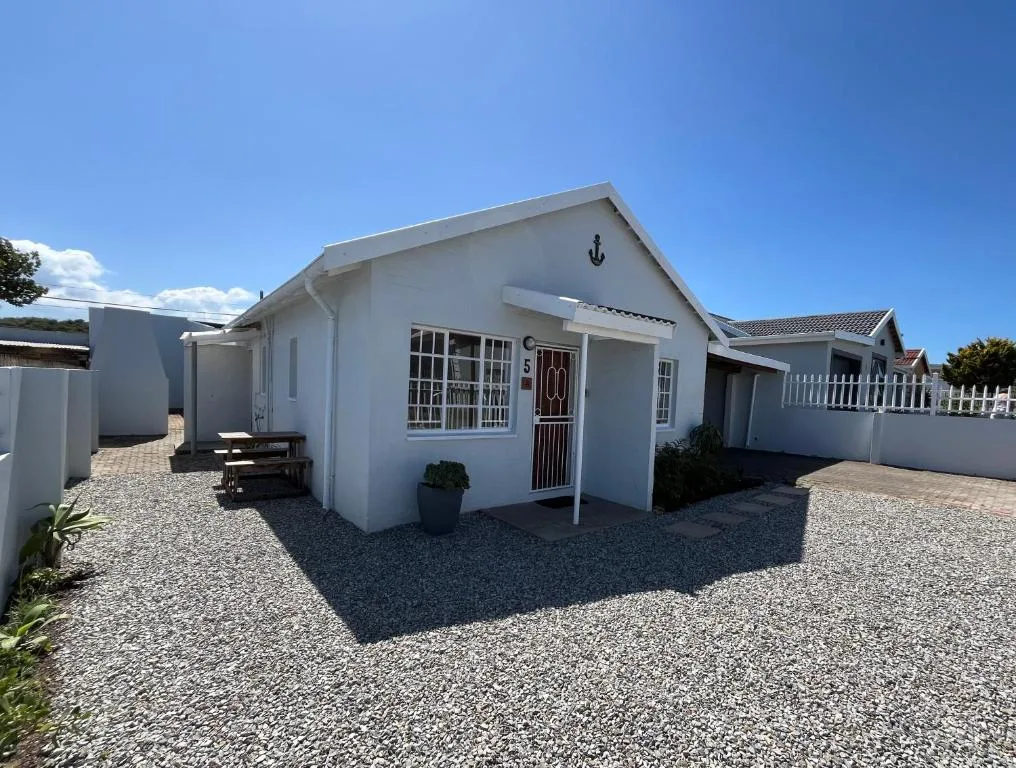 White cottage with anchor symbol, gravel courtyard, and white fence