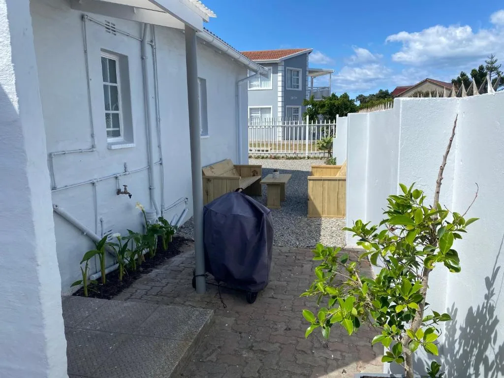 White-walled property entrance with braai area and wooden benches visible