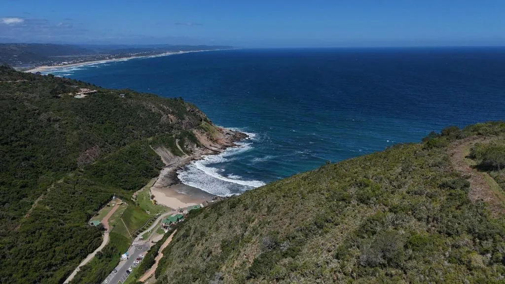 Dramatic coastal panorama with golden beach, crashing waves, and distant coastline