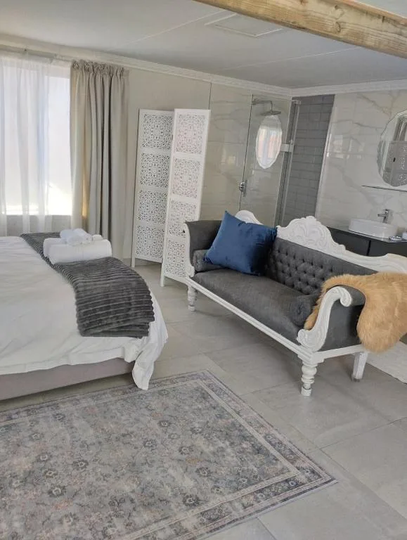 Modern bedroom with white bed, gray upholstered seating, and ensuite bathroom visible