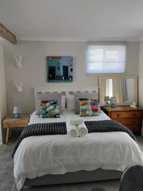 Bright bedroom with white bed, colorful pillows, wooden nightstand, and mirror