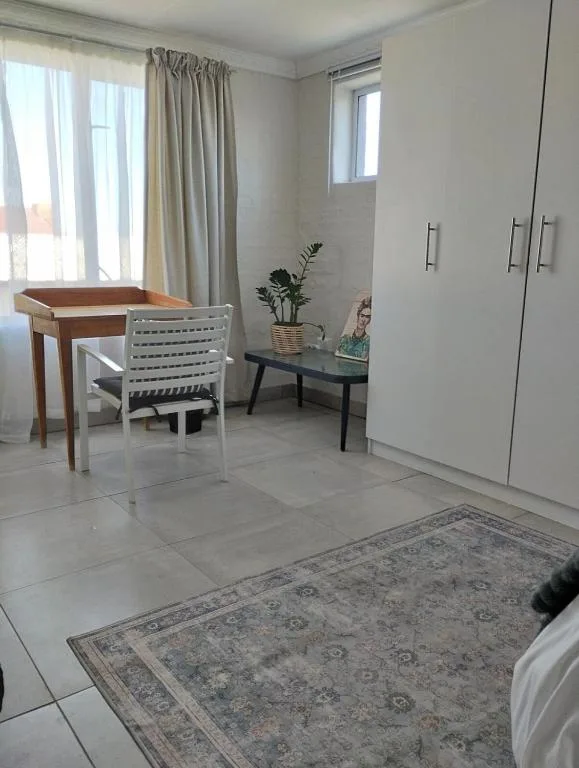 Bright bedroom with desk, chair, wardrobe, and large windows overlooking garden