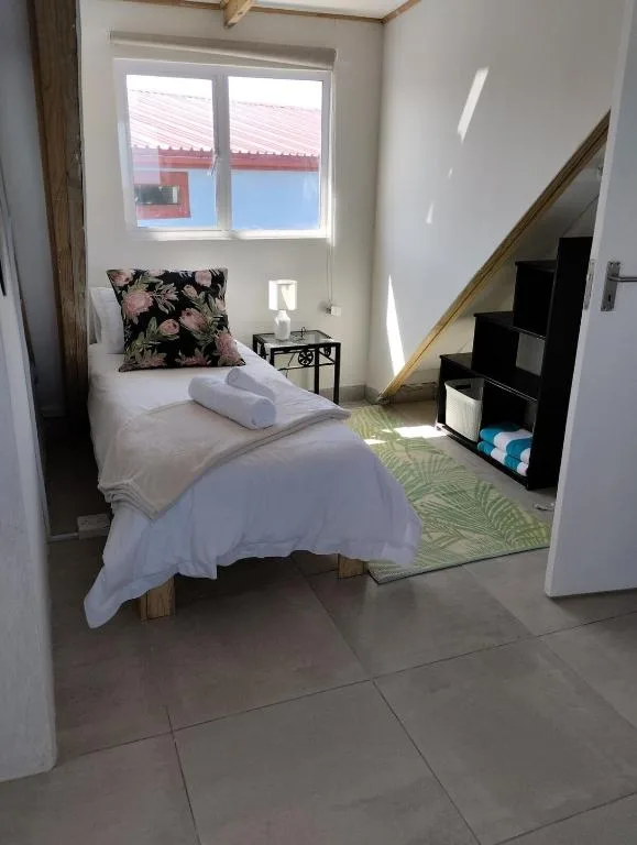 Bright bedroom with single bed, floral cushion, and staircase access