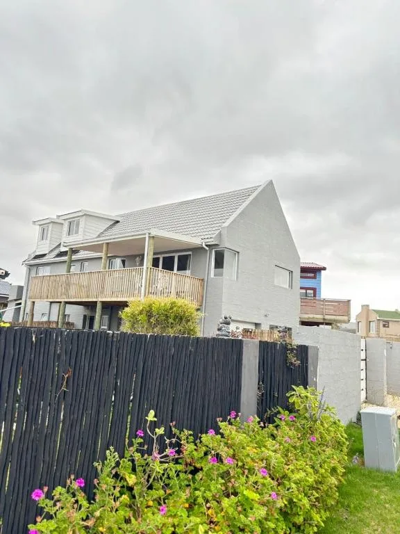 Modern white cottage with deck, black fence and blooming garden flowers