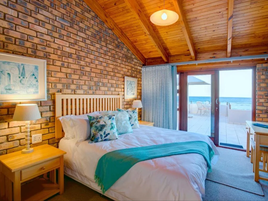 Spacious bedroom with exposed brick walls, wooden ceiling, and ocean view doors