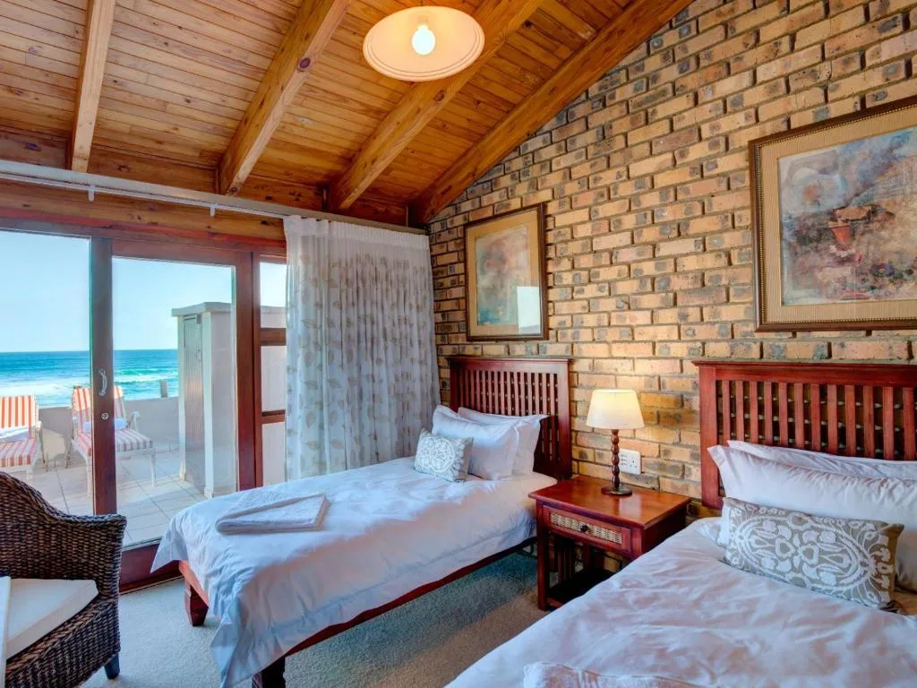 Spacious bedroom with two beds, ocean view through glass doors, wooden ceiling